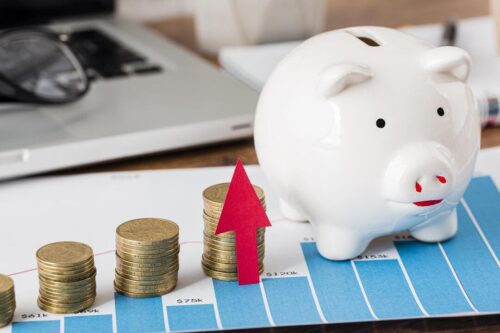 fundos de renda fixa: um cofrinho de porco, um gráfico mostrando as oscilações do mercado e várias pilhas de moedas e uma seta para cima.