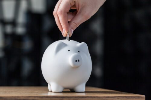 Uma mulher guarda moedas em um cofre de porquinho e pode estar se questionando se a poupança vale a pena