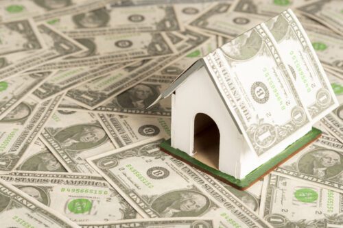 reits: várias notas de dólares no chão e uma casinha com um telhado feito com uma nota de dólar.