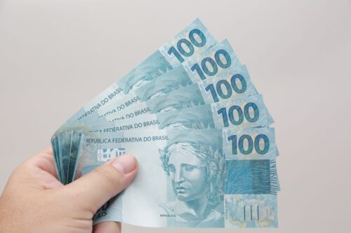 onde investir 50 mil: uma mão segurando notas de 100 reais.