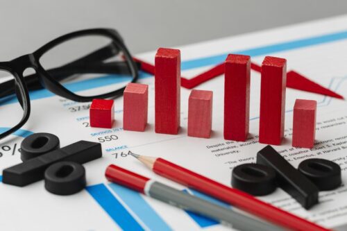 IGP-M: composição com óculos, gráfico em vermelho, símbolos de porcentagem e lápis sobre um papel branco com gráficos em azul