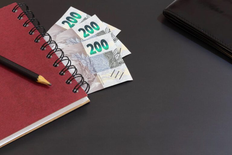 rendimento poupança: uma agenda de capa vermelha com três notas de 200 reais.