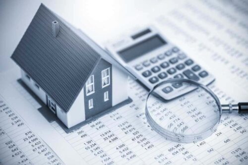 quanto rende um fundo imobiliário: A imagem está em escala de cinza, representando uma casa e ao lado uma calculadora e uma lupa.