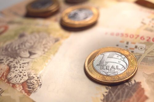 real digital: como plano de fundo uma nota de 50 reais e algumas moedas de um real por cima da nota.