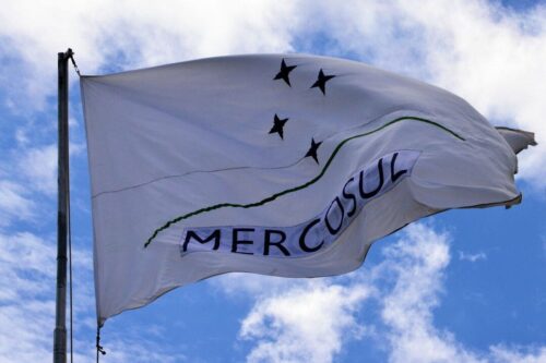mercosul: uma bandeira branca escrito Mercosul em preto e um sombreado azul por cima das letras.