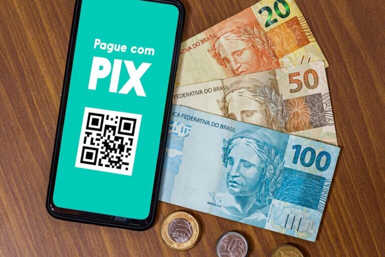 PIX: um celular com uma informação para realizar um pagamento via pix e uma nota de 20 reais, 50 reais e 100 reais e algumas moedas ao lado.