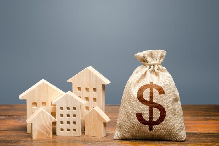 Especulação imobiliária: um saco com um símbolo de $ e umas casas de madeira em volta.