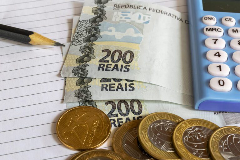 impostos: três notas de 200 reais mais algumas moedas de um real e uma de vinte e cinco centavos e um lápis mais uma folha de caderno.