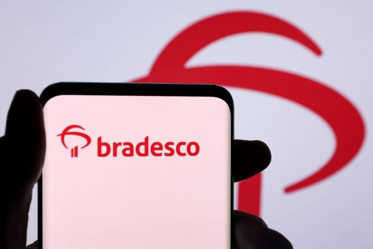 Smartphone com logo do Bradesco (BBDC4) em primeiro plano e fundo desfocado com logo maior.