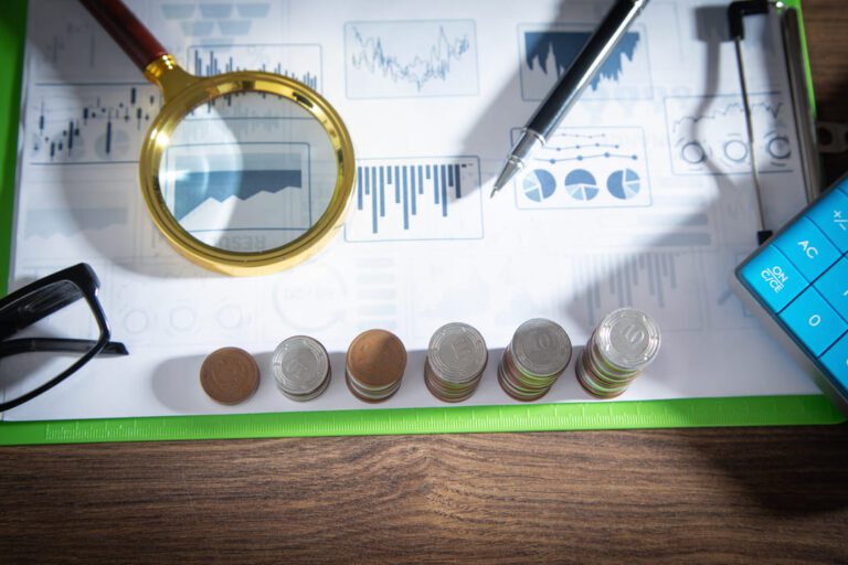 Moedas empilhadas, lupa, óculos e caneta sobre uma folha de gráficos que demonstram o rating de crédito.