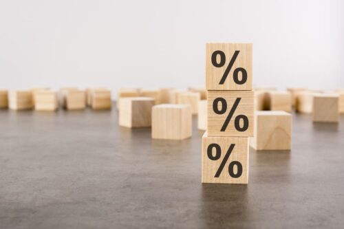 Cubos de madeira com ilustração do símbolo de porcentagem empilhados, representando a alíquota do Imposto de Renda.