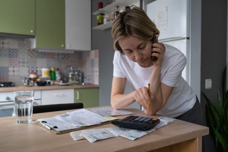 Mulher falando ao telefone e usando calculadora enquanto examina papéis sobre a mesa, representando a amortização de dívidas.