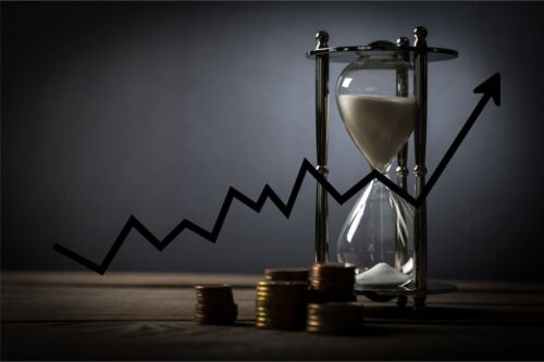 Ampulheta e moedas empilhadas em mesa com seta indicando aumento, representando o breakeven na bolsa de valores.