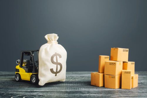 Miniatura de empilhadeira carregando saco de dinheiro, caixas de produtos estão empilhadas ao lado, representando o BTLG11, fundo imobiliário de logística.