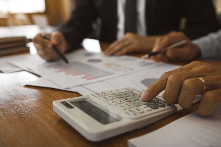 Dois homens de roupa social analisando folhas e utilizando a calculadora para calcular e declarar o IRPJ.