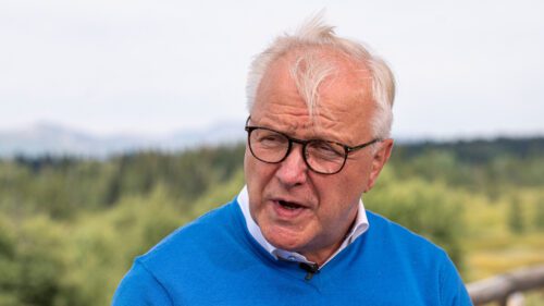 Olli Rehn de blusa azul em fundo de gramado desfocado