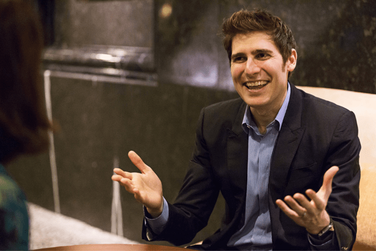 Eduardo Saverin, cofundador do facebook, sorri com braços abertos durante entrevista.