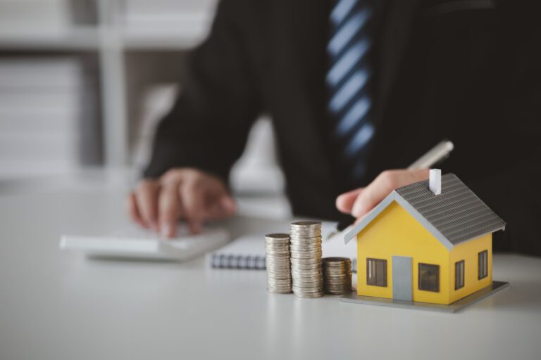 Executivo trabalhando em cálculos financeiros com modelo de casa e moedas, simbolizando investimento HABT11.