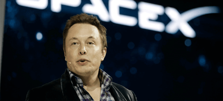 Elon Musk falando na frente de um painel luminoso