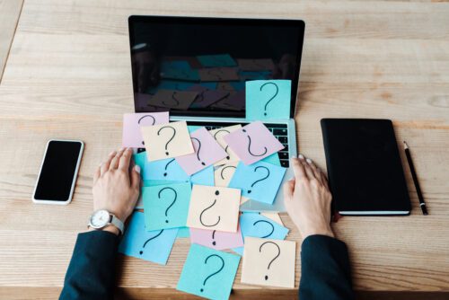 Notebook coberto por cartões com pontos de interrogação. Afinal, é melhor abrir uma franquia ou investir em negócio prórpio