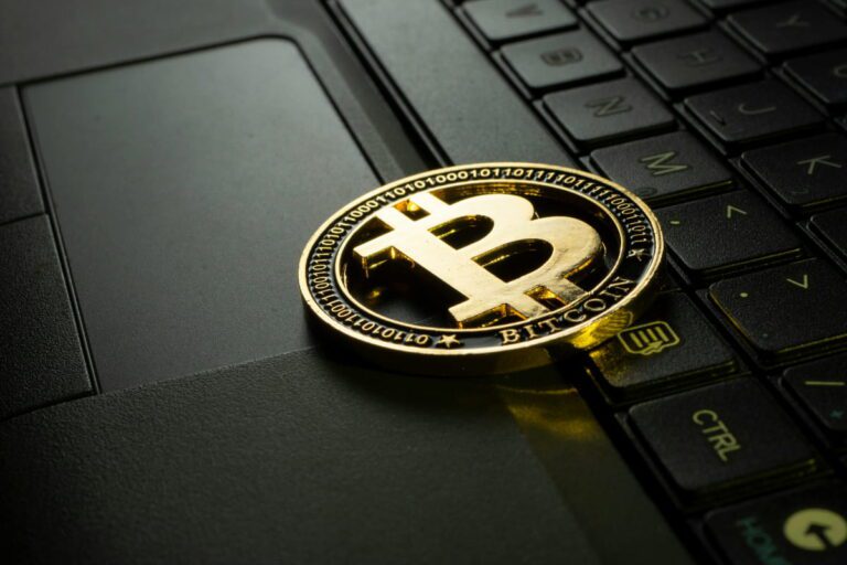 Moeda Bitcoin em um teclado de laptop, ilustrando os conceitos de Proof of Work e Proof of Stake.