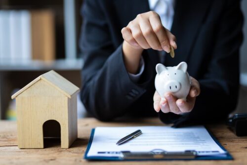 Pessoa colocando moeda em cofrinho, com miniatura de casa ao lado, simbolizando os melhores fundos imobiliários de 2024.