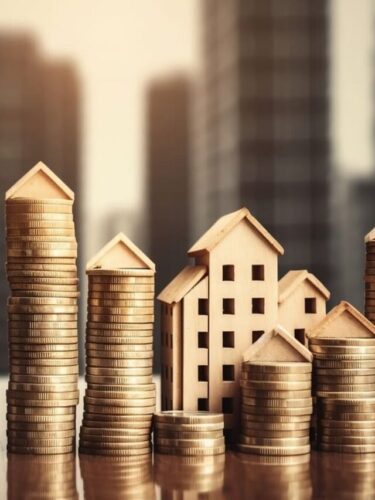 Pilha de moedas com miniaturas de casas, representando fundos imobiliários baratos para investir.