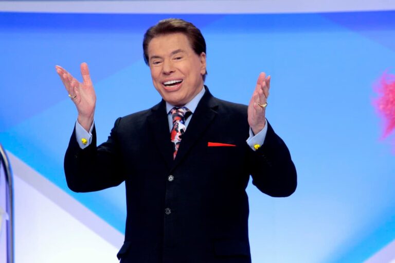 Silvio Santos sorrindo e gesticulando com as mãos durante a gravação de seu programa de televisão em estúdio.