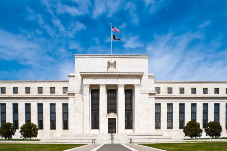 Fachada do edifício principal do Sistema de Reserva Federal dos Estados Unidos em Washington, D.C., com bandeiras hasteadas.