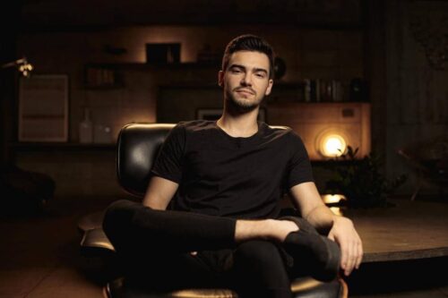 Imagem de Breno Perrucho sentado em uma cadeira, vestindo uma camisa preta, referência no mercado de investimentos.