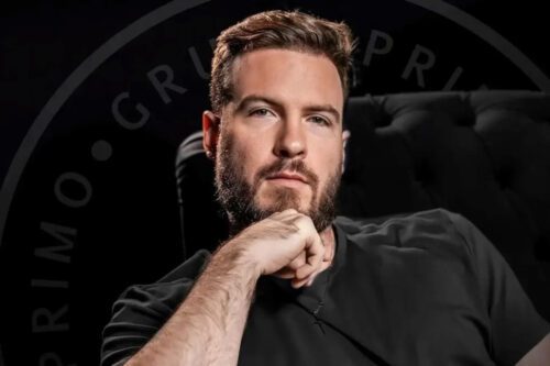 Thiago Nigro, fundador do 'Primo Rico', sentado com expressão pensativa e fundo escuro, destacando seu sucesso como influenciador financeiro.