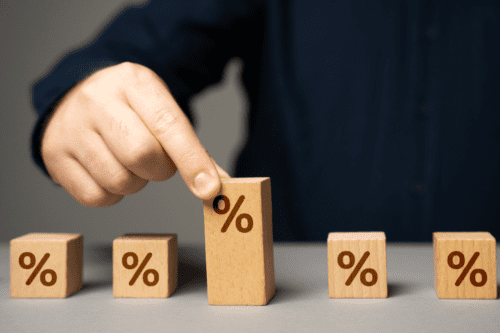 Empresário segurando blocos de porcentagens, simbolizando o impacto da alta da taxa de juros em fundos imobiliários (FIIs).