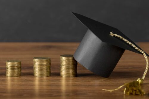 Pilhas de moedas com chapéu de formatura, representando o crescimento financeiro, ideal para empresas do setor de educação para investir.