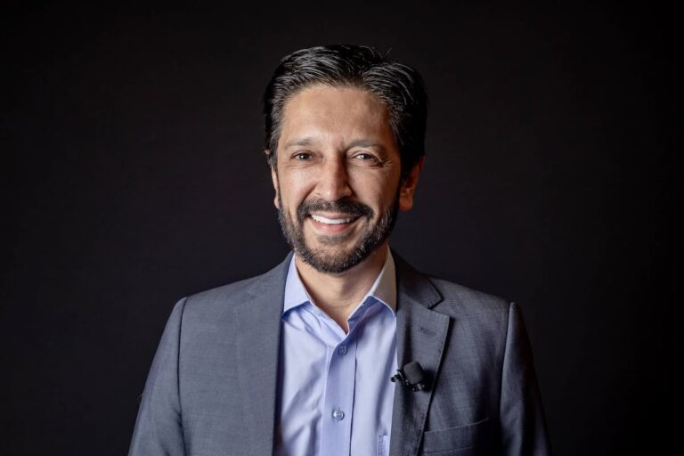 Ricardo Nunes sorrindo, usando terno e gravata, posando em fundo escuro. Prefeito de São Paulo e figura pública política em destaque.