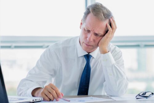 Homem pensativo com expressão preocupada, analisando documentos, representando conceito de nome em protesto em cenário corporativo.