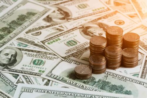 Pilhas de moedas e notas de dólar dos EUA simbolizando a alta do dólar hoje com foco nos decretos de Donald Trump.