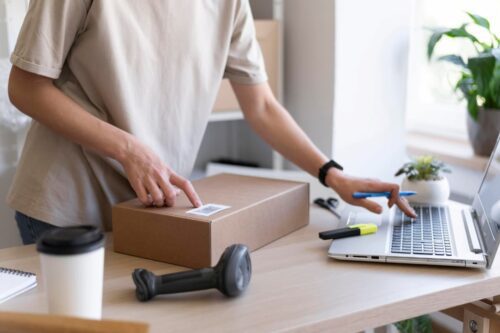 Pessoa preparando encomenda para envio enquanto verifica informações no laptop, representando o modelo de negócio dropshipping.