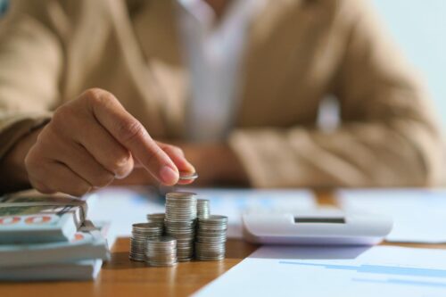 Pessoa empilhando moedas com papéis e calculadora ao fundo, representando opções para decidir onde investir 10 mil reais.