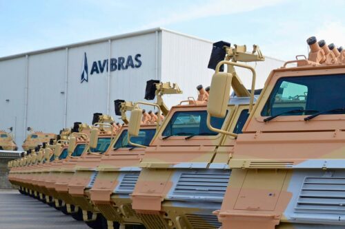 Veículos militares enfileirados em frente à fábrica da Avibras, destacando a indústria de defesa e o impacto nas ações da Avibras.