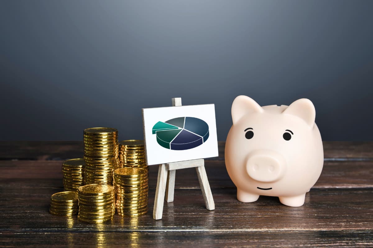 Cofrinho, pilhas de moedas e gráfico representam investimentos. "Se eu investir 1.000 reais no Tesouro Direto, quanto rende?"