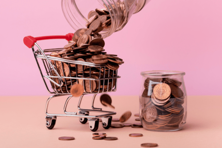 m minicarrinho de supermercado de metal sendo preenchido por moedas douradas que caem de um pote de vidro virado.