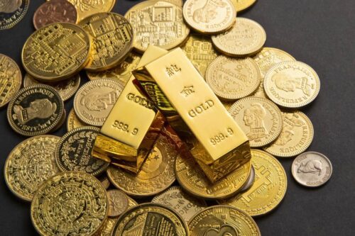 Barra de ouro puro 999.9 cercada por moedas douradas, representando quanto custa uma barra de ouro em 2025 no mercado atual.