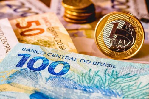 Pilha de moedas e cédulas de dinheiro, representando que a taxa de juros de longo prazo caem.