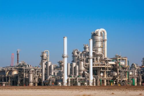 Refinaria de petróleo sob céu azul, ilustrando cenário em que o petróleo hoje cai devido a fatores econômicos e geopolíticos.