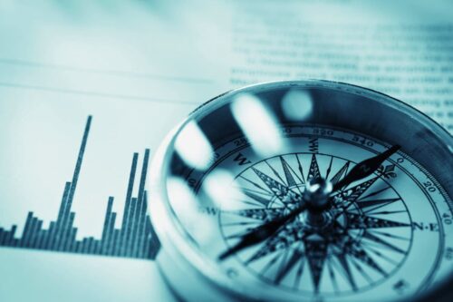 Bússola sobre gráficos financeiros ilustrando o que é guidance nos investimentos e sua função como orientação estratégica.