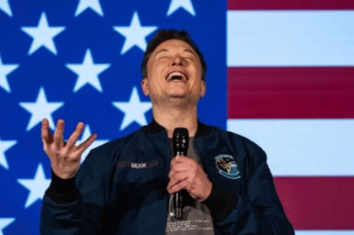 Elon Musk rindo com a bandeira dos Estados Unidos ao fundo, em cena relacionada às ações da Tesla que despencaram após embate público com Donald Trump.