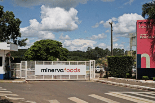 Imagem da entrada da Minerva Foods, destacando o impacto do aumento de capital na redução do risco financeiro da empresa, segundo o Citi, com cenário de céu azul e nuvens.
