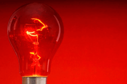 Imagem de uma lâmpada incandescente com luz vermelha intensa, simbolizando a bandeira vermelha na conta de luz já está valendo, alertando para aumento de tarifas de energia.