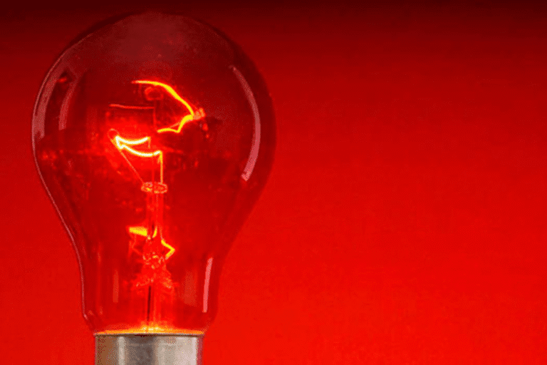 Imagem de uma lâmpada incandescente com luz vermelha intensa, simbolizando a bandeira vermelha na conta de luz já está valendo, alertando para aumento de tarifas de energia.