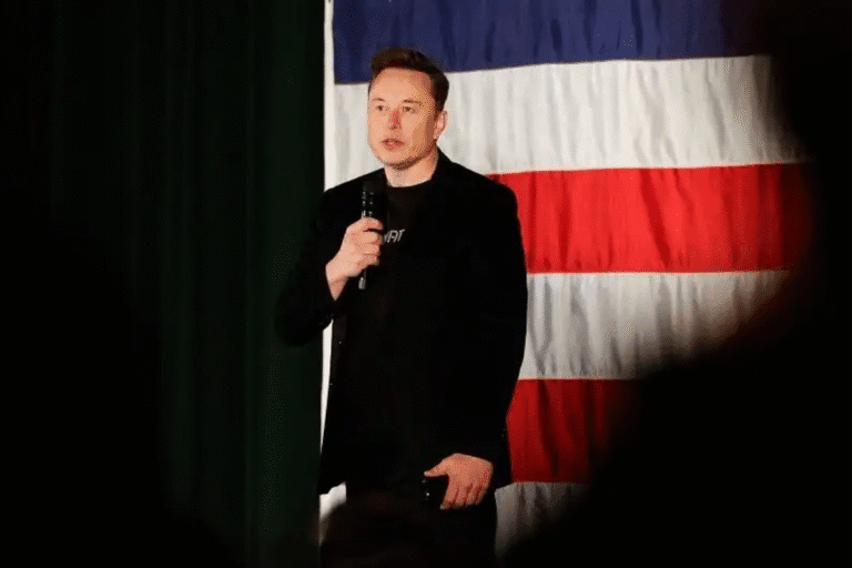 Elon Musk durante um evento com bandeira americana ao fundo, ilustrando o impacto de um confronto com Donald Trump que levou à perda de R$150 bilhões e afetou as ações da Tesla.